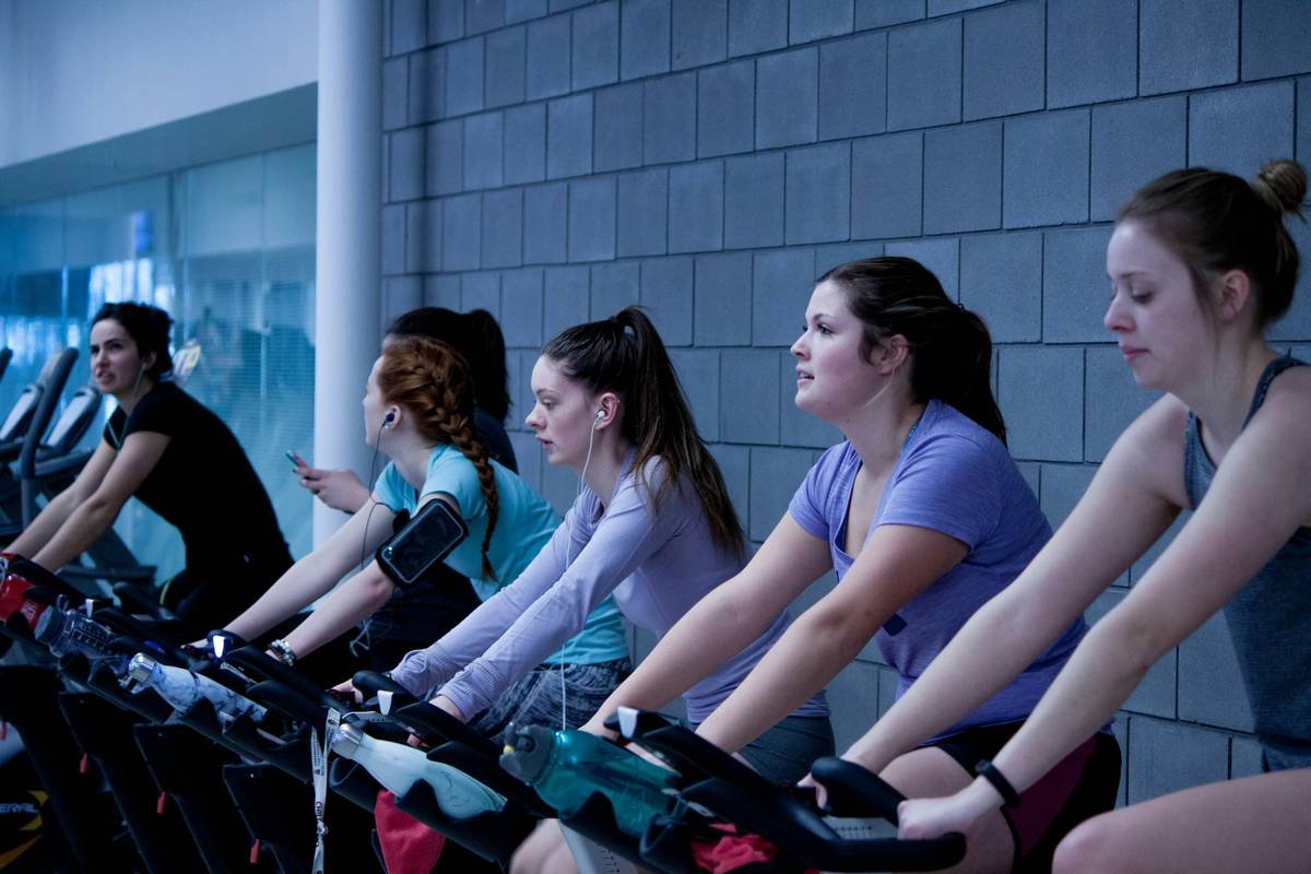 A woman doing an energetic spin bike workout indoors, wearing athletic gear, with sweat dripping off her face.