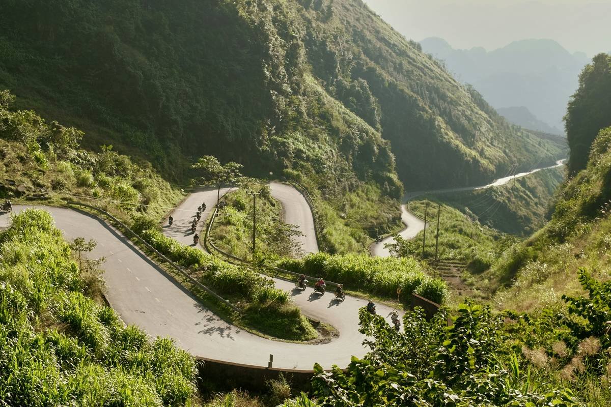 A dramatic aerial-style view of a winding mountain road snaking through lush, emerald-green hills during a high-altitude road trip.