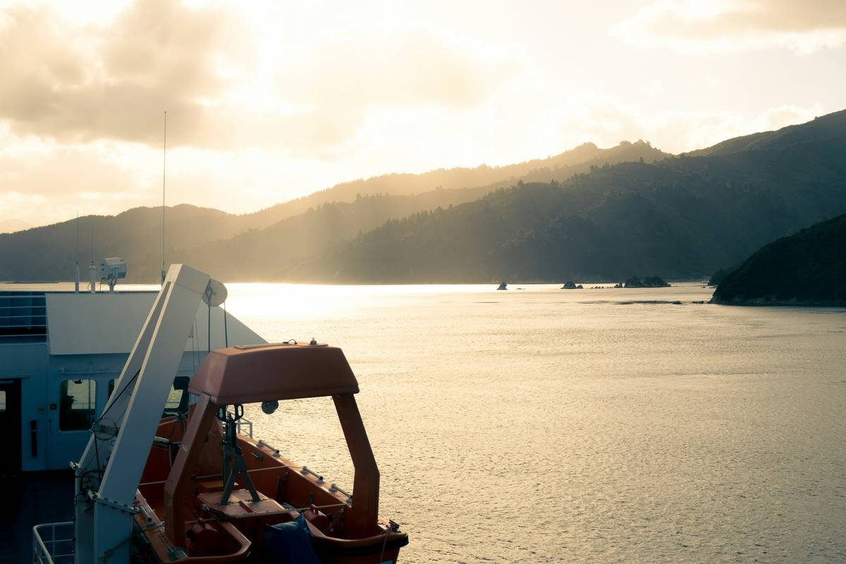 Sunset over a calm sea with mountains from a ship.